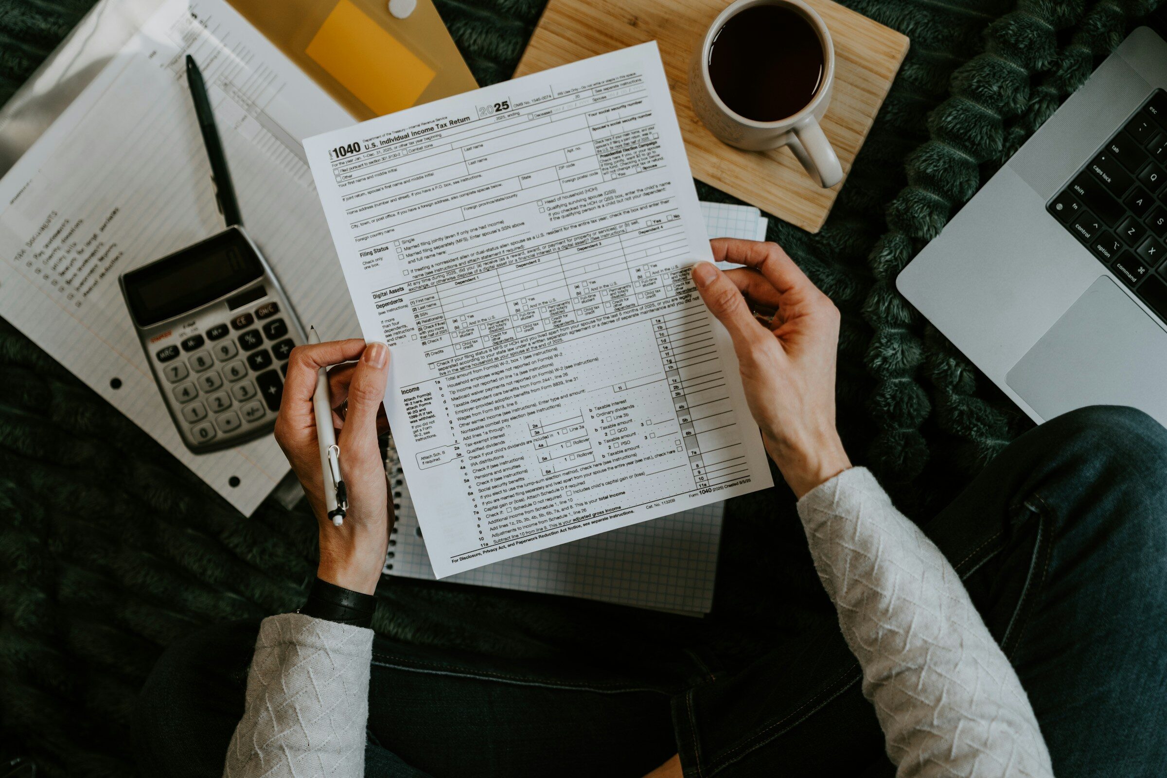 Hands holding tax forms beside a calculator and laptop