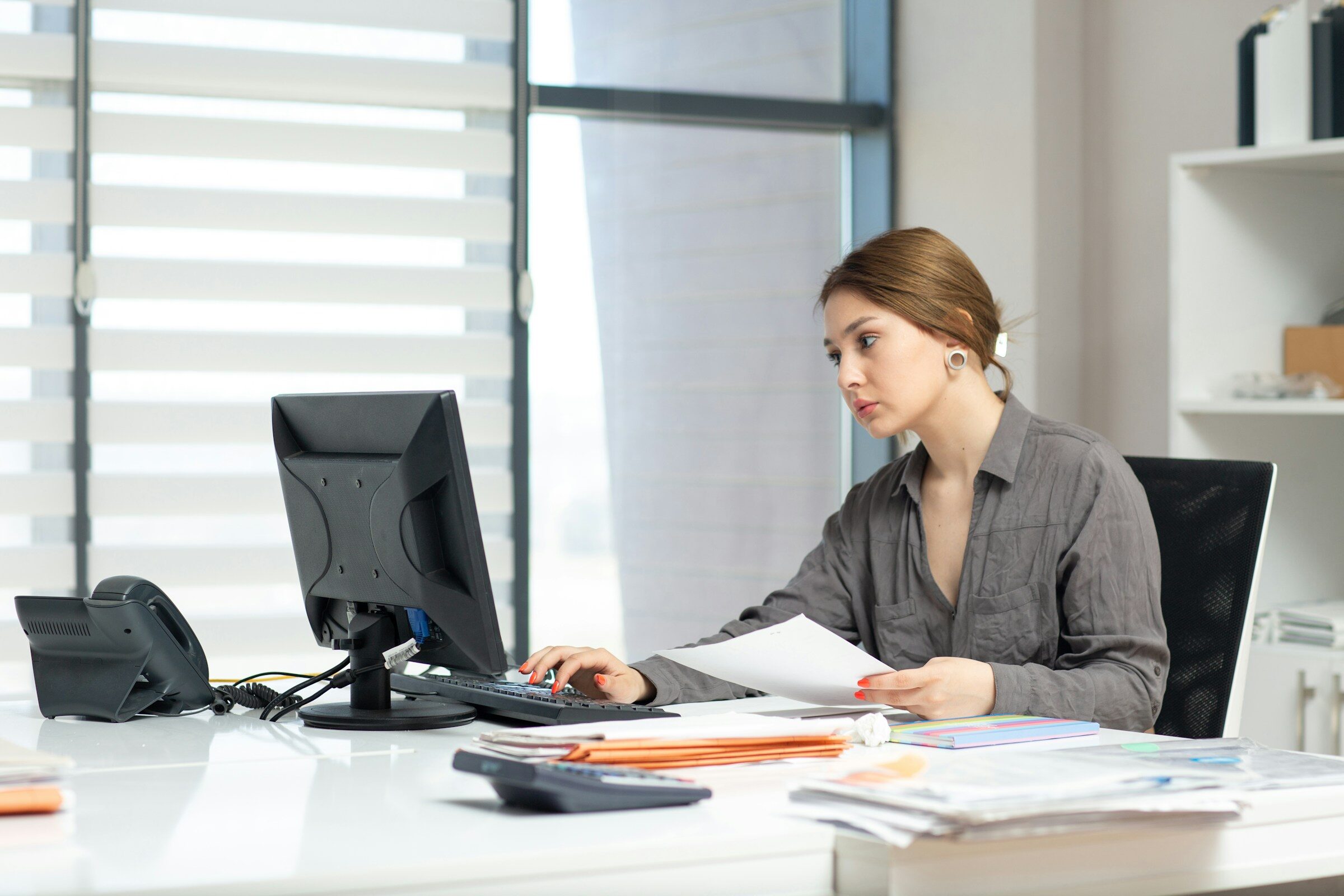 A woman working on a computer and documents at an office desk