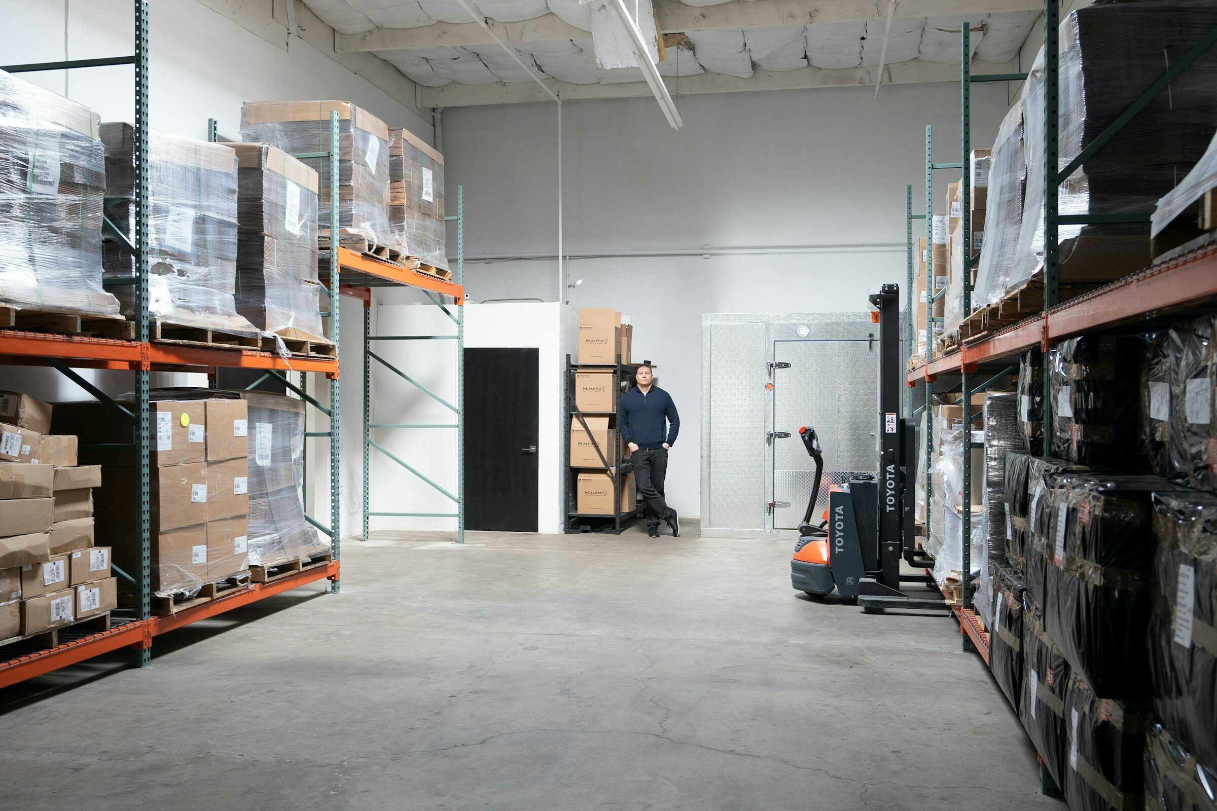 A warehouse worker beside a forklift in a distribution unit