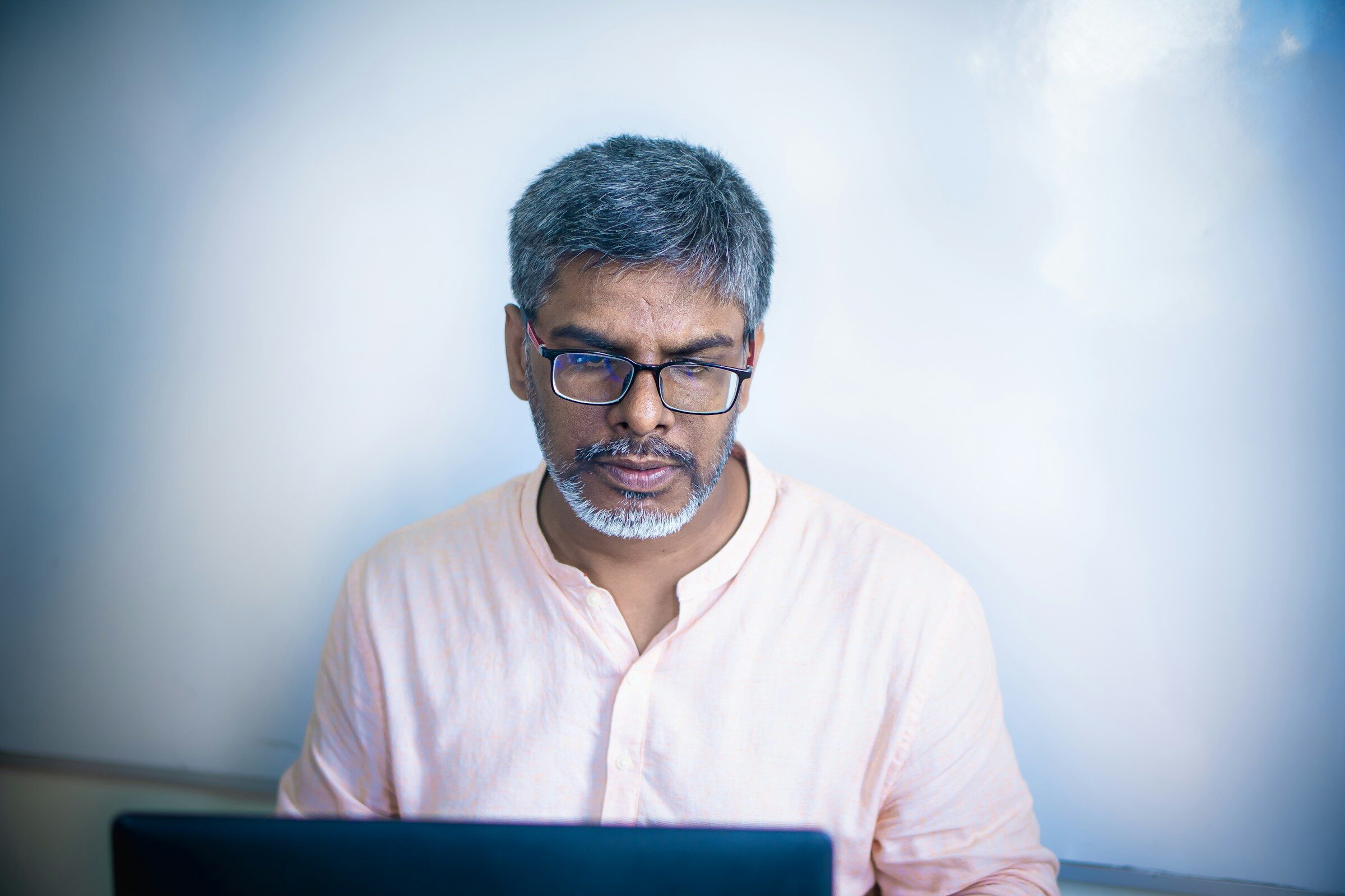 A man in glasses looking down at a laptop