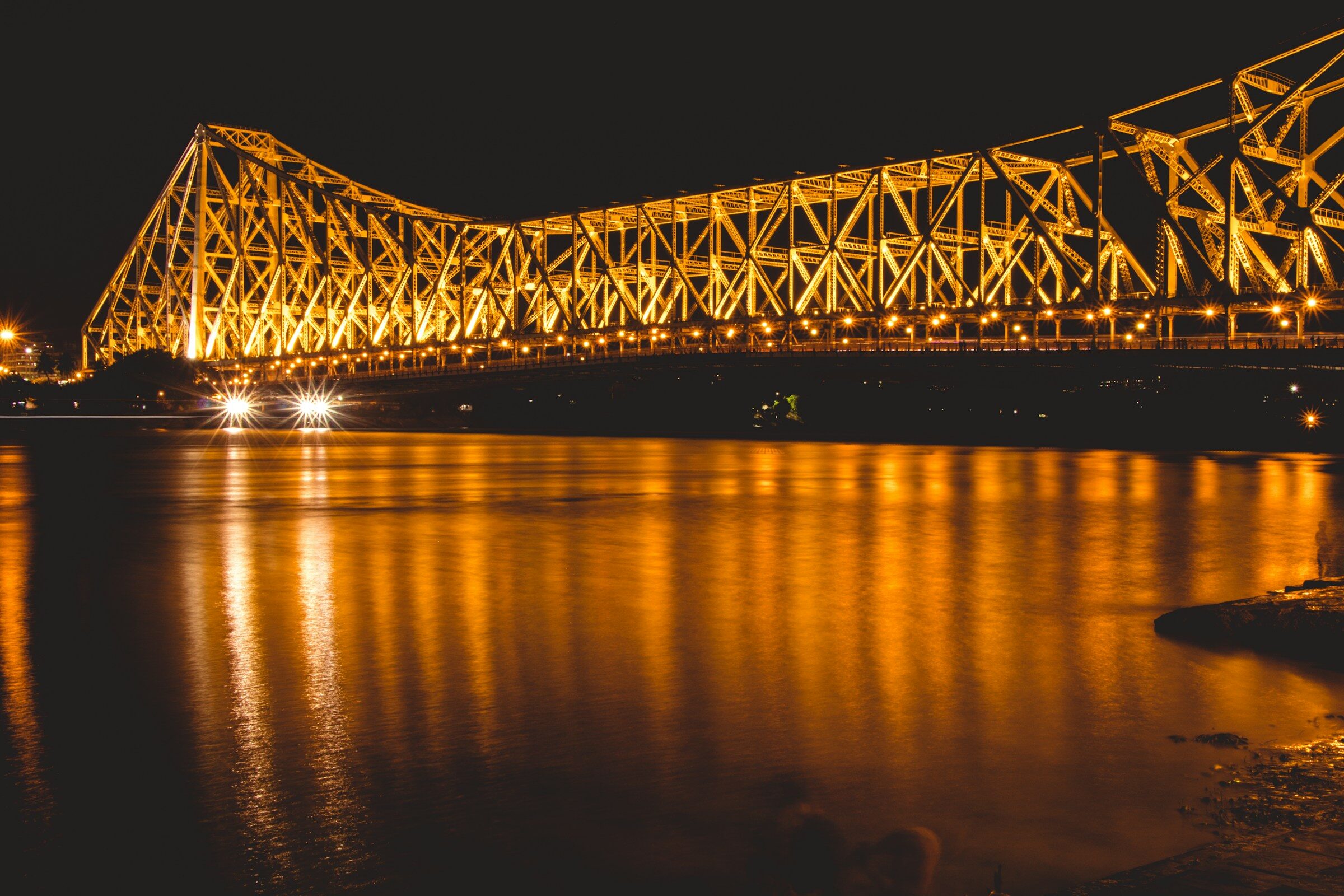 Howrah Bridge lit gold at night, reflected in the Hooghly