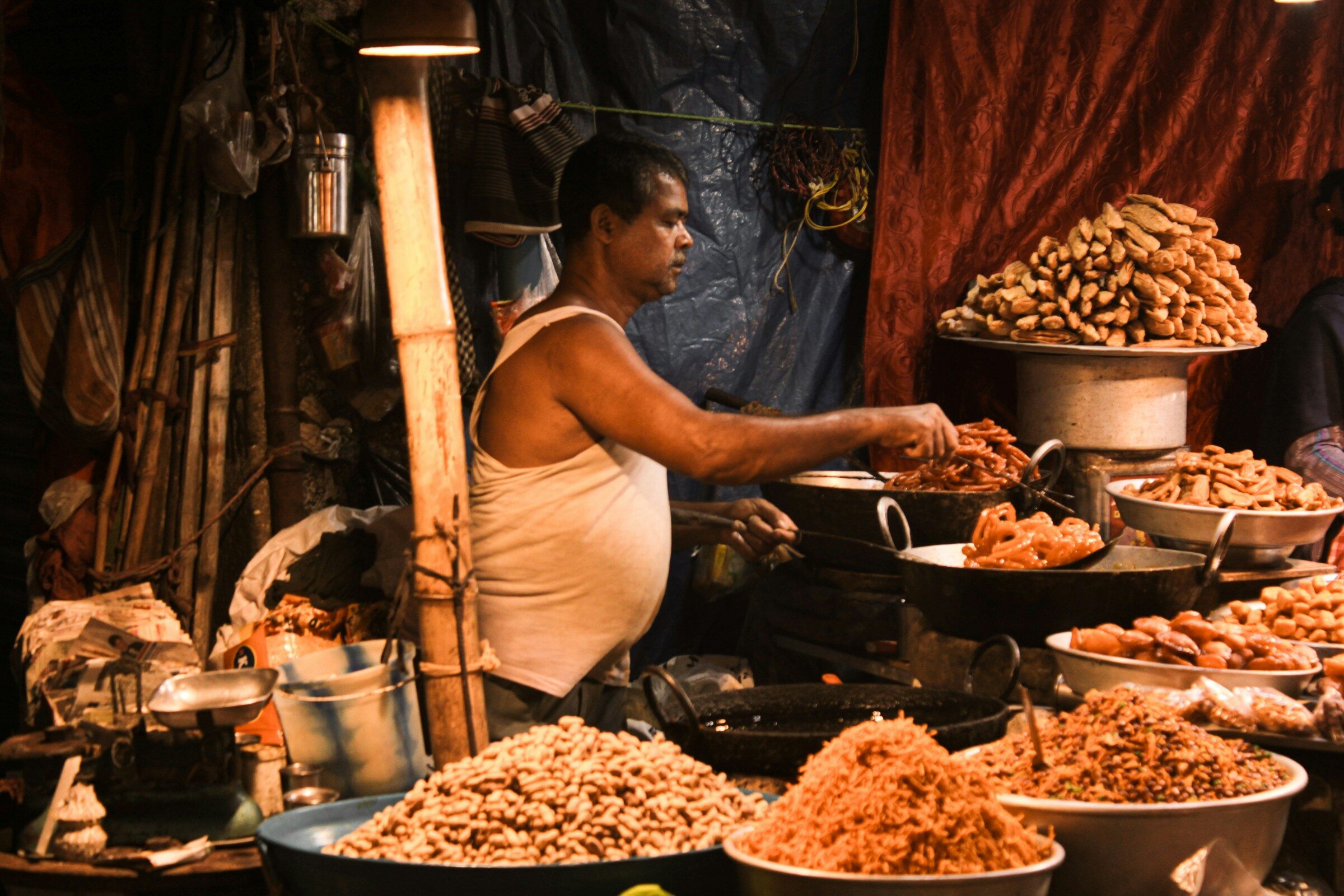 A man at a table filled with food in a Kolkata market