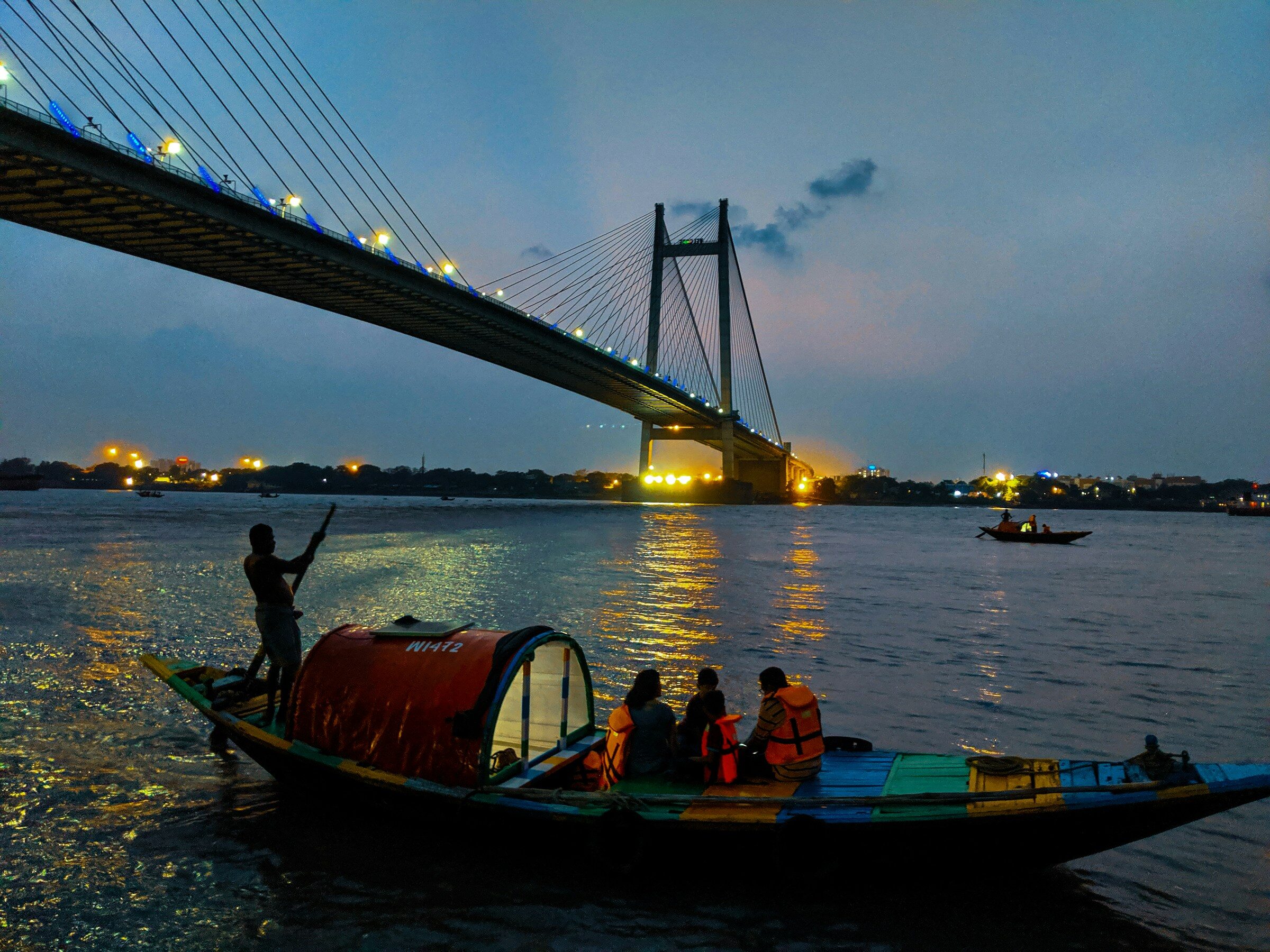 A wooden boat rowed with passengers under the Vidyasagar Setu at dusk
