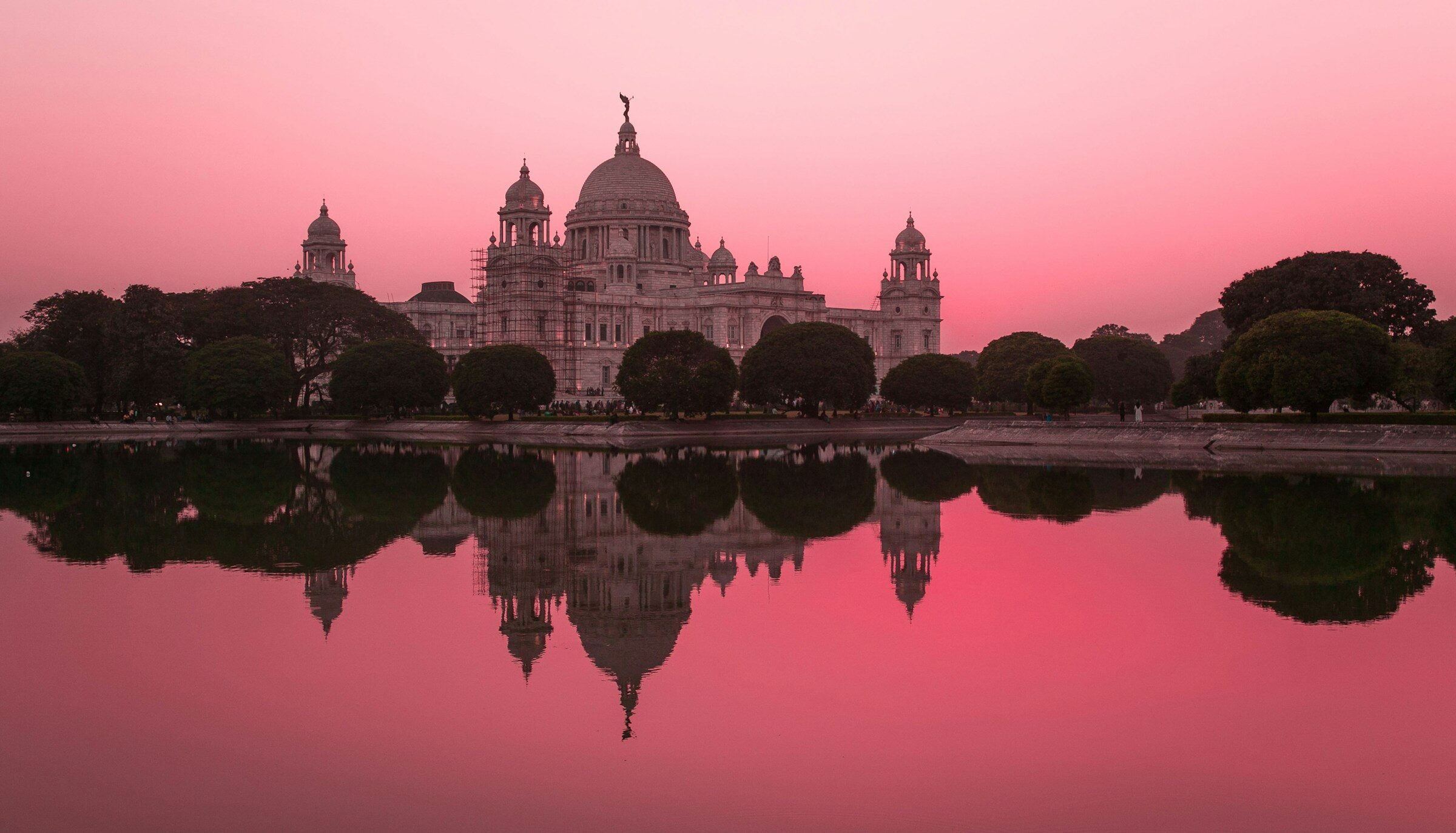 The Victoria Memorial reflected in still water under a pink sky
