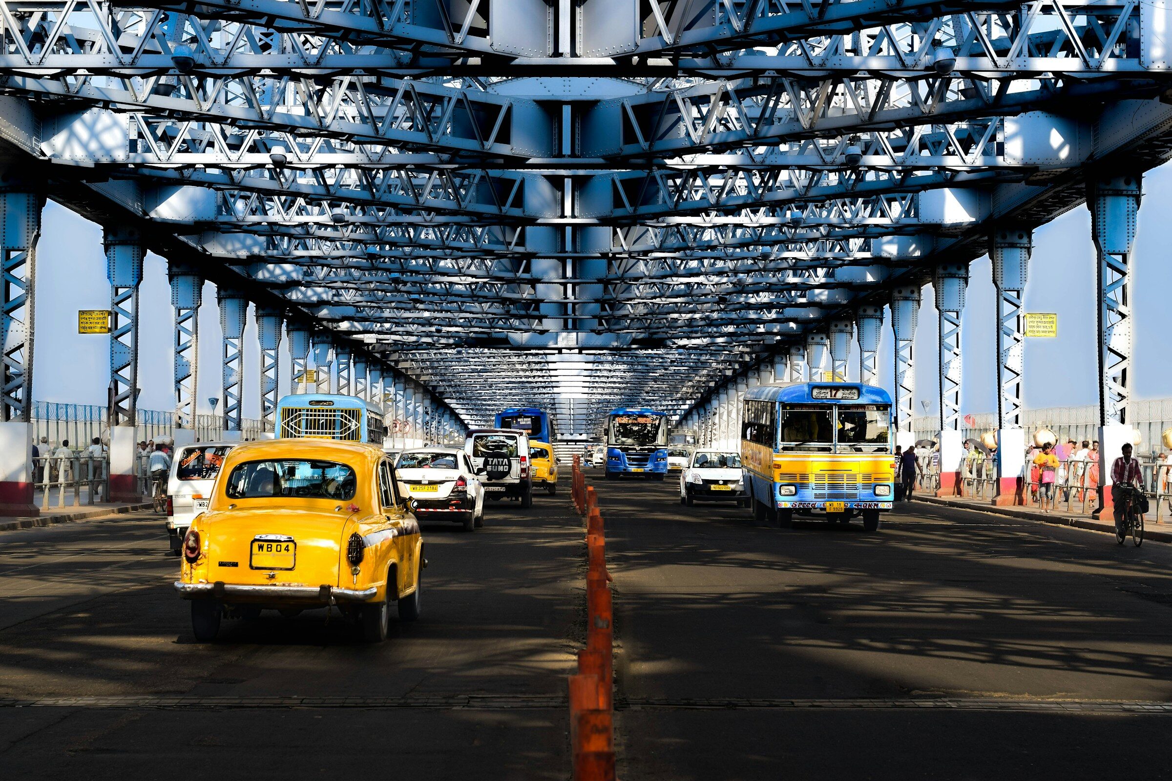 Yellow taxis crossing beneath the steel lattice of Howrah Bridge