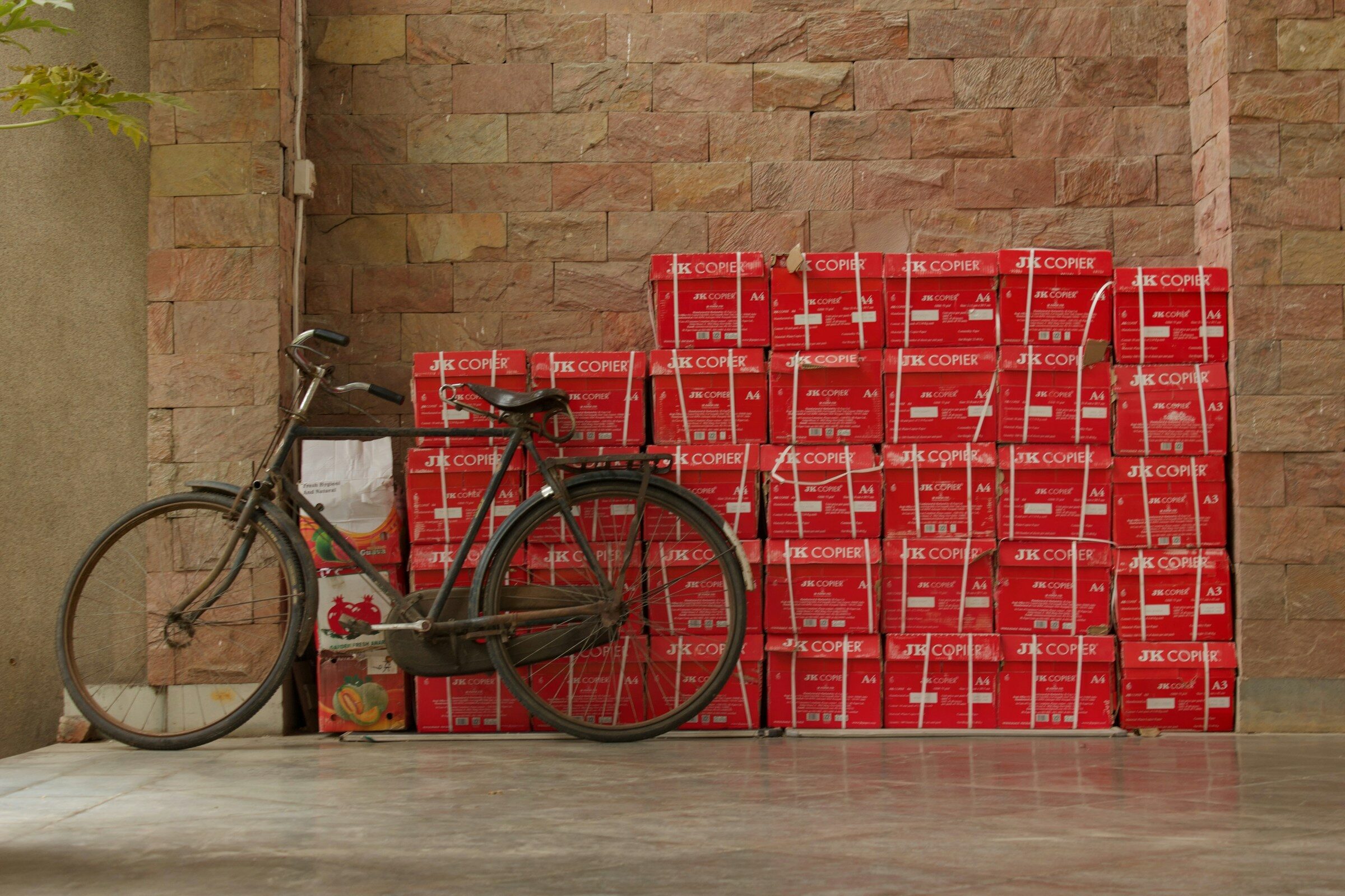 A delivery bicycle leaning against a stack of red parcel boxes