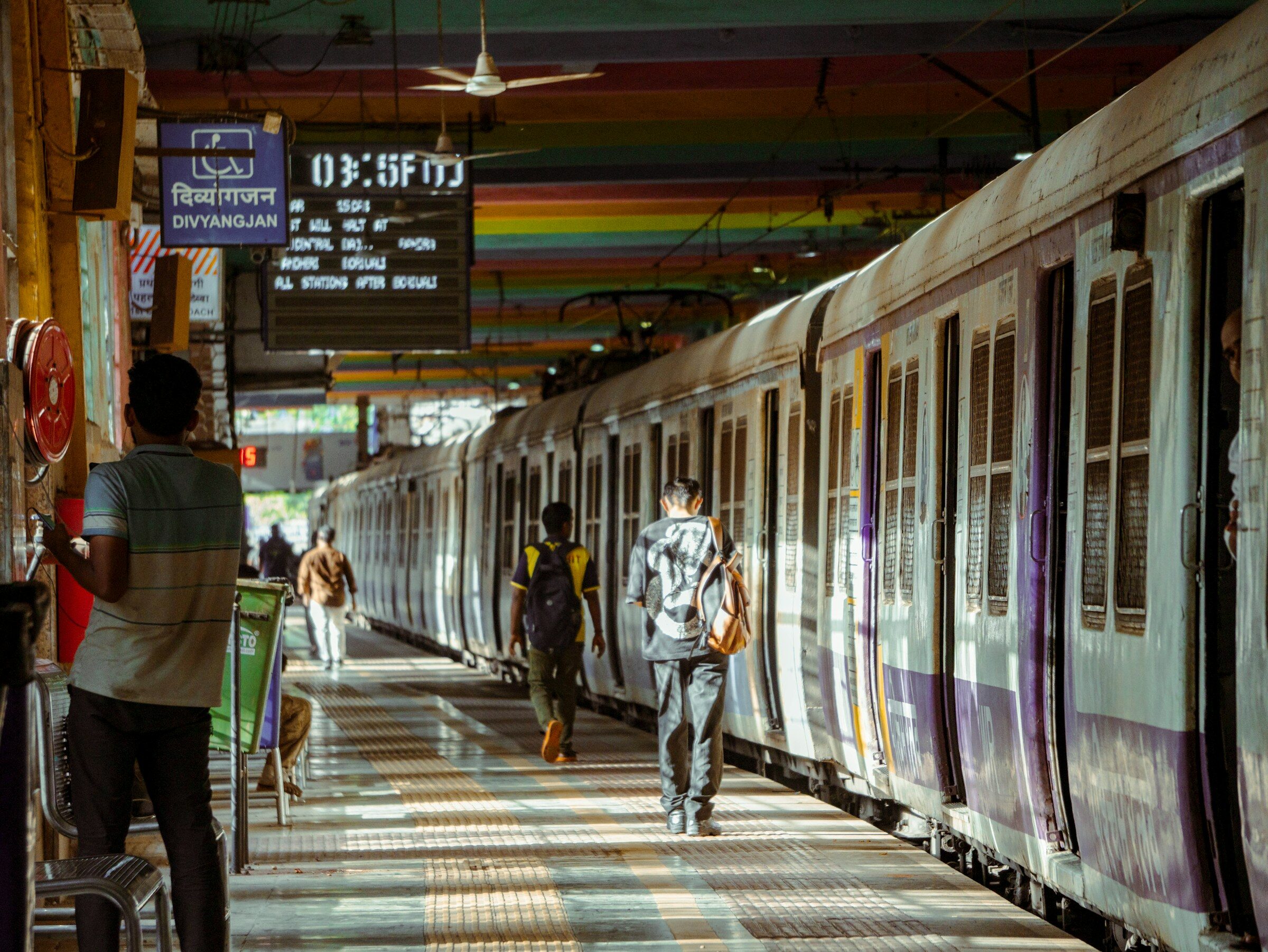 Commuters walking along a Mumbai station platform beside a local train