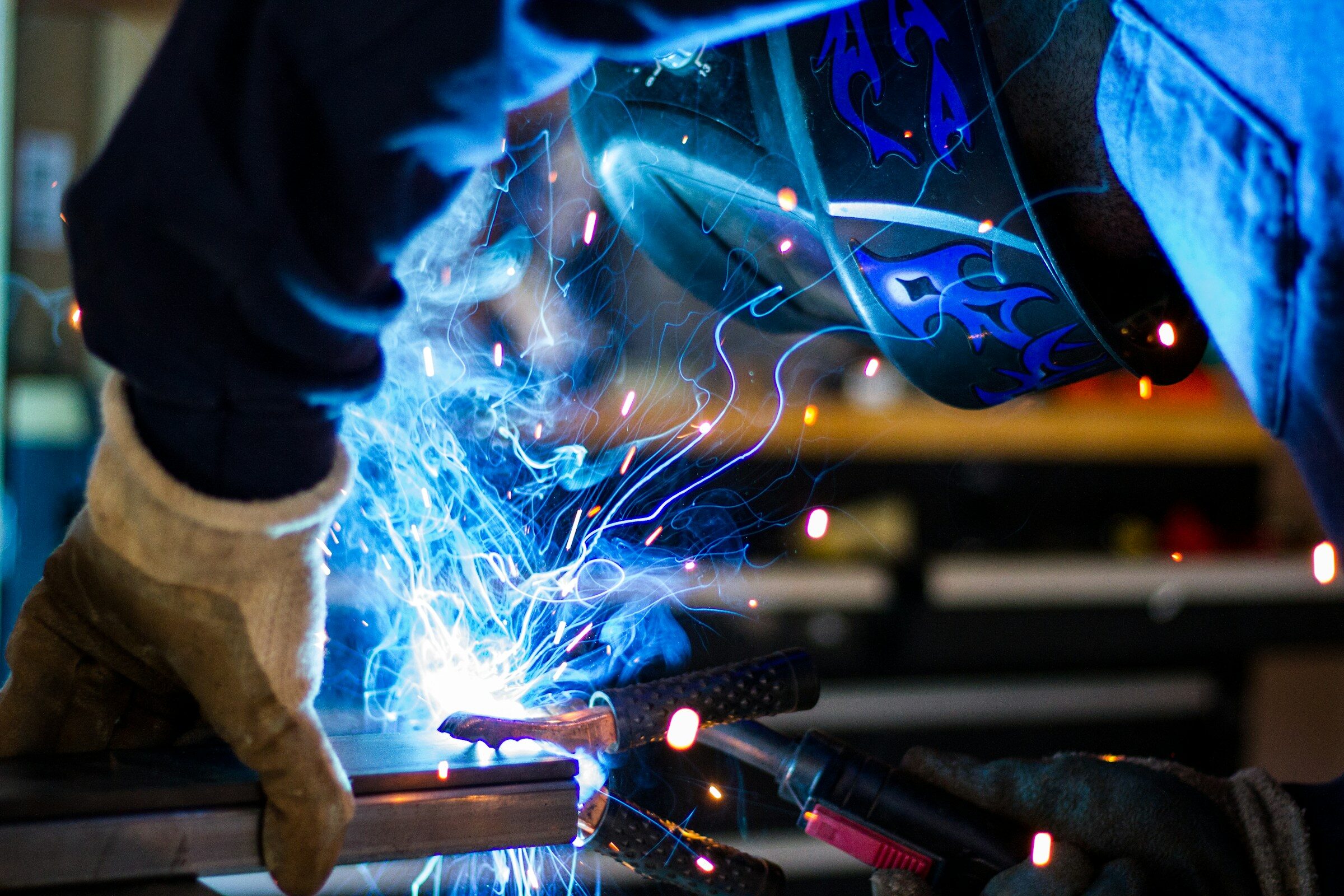 Welder in protective helmet and gloves working steel